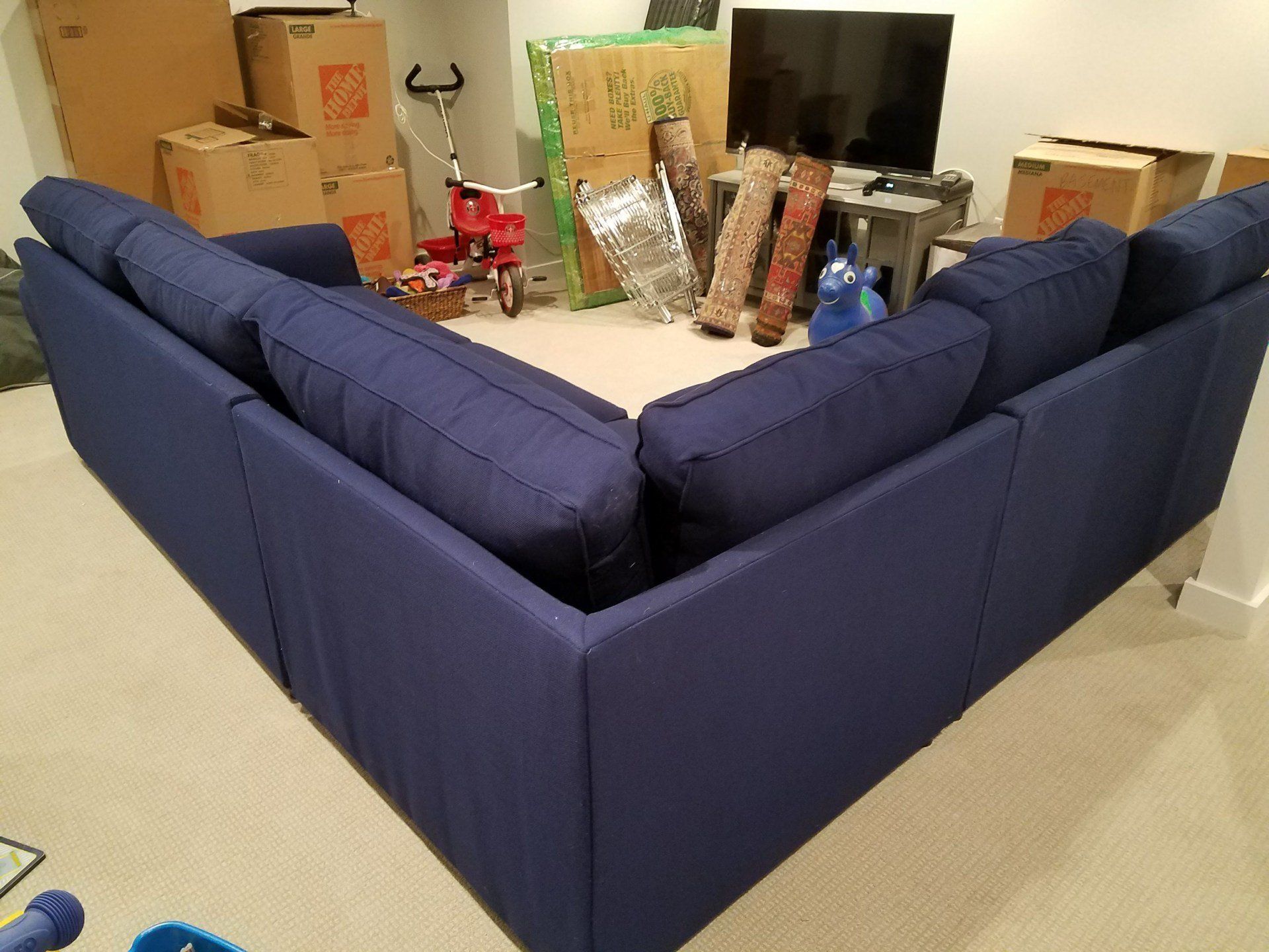 A blue sectional couch in a living room surrounded by boxes
