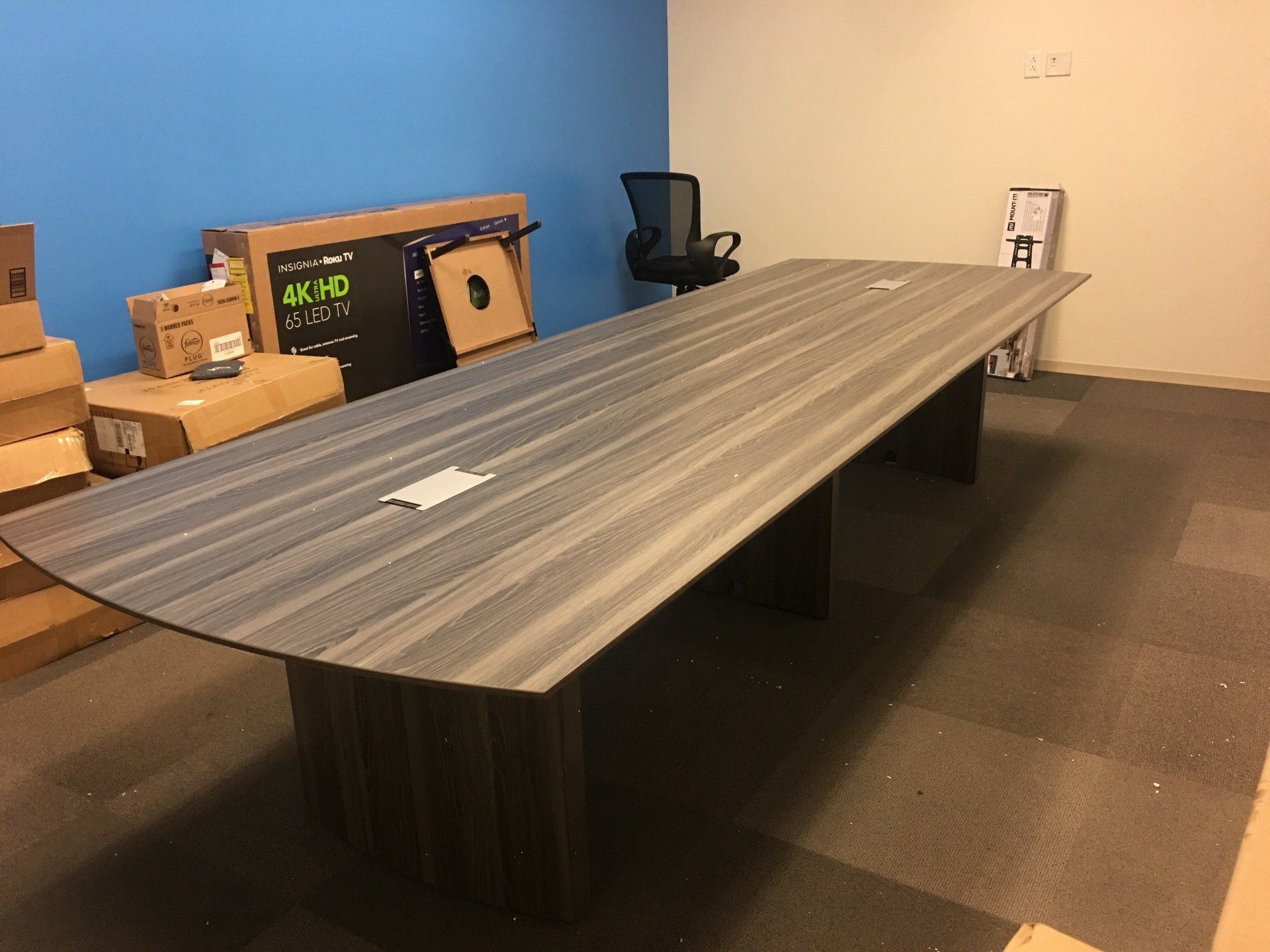 A long conference table is sitting in a room with boxes on the wall.