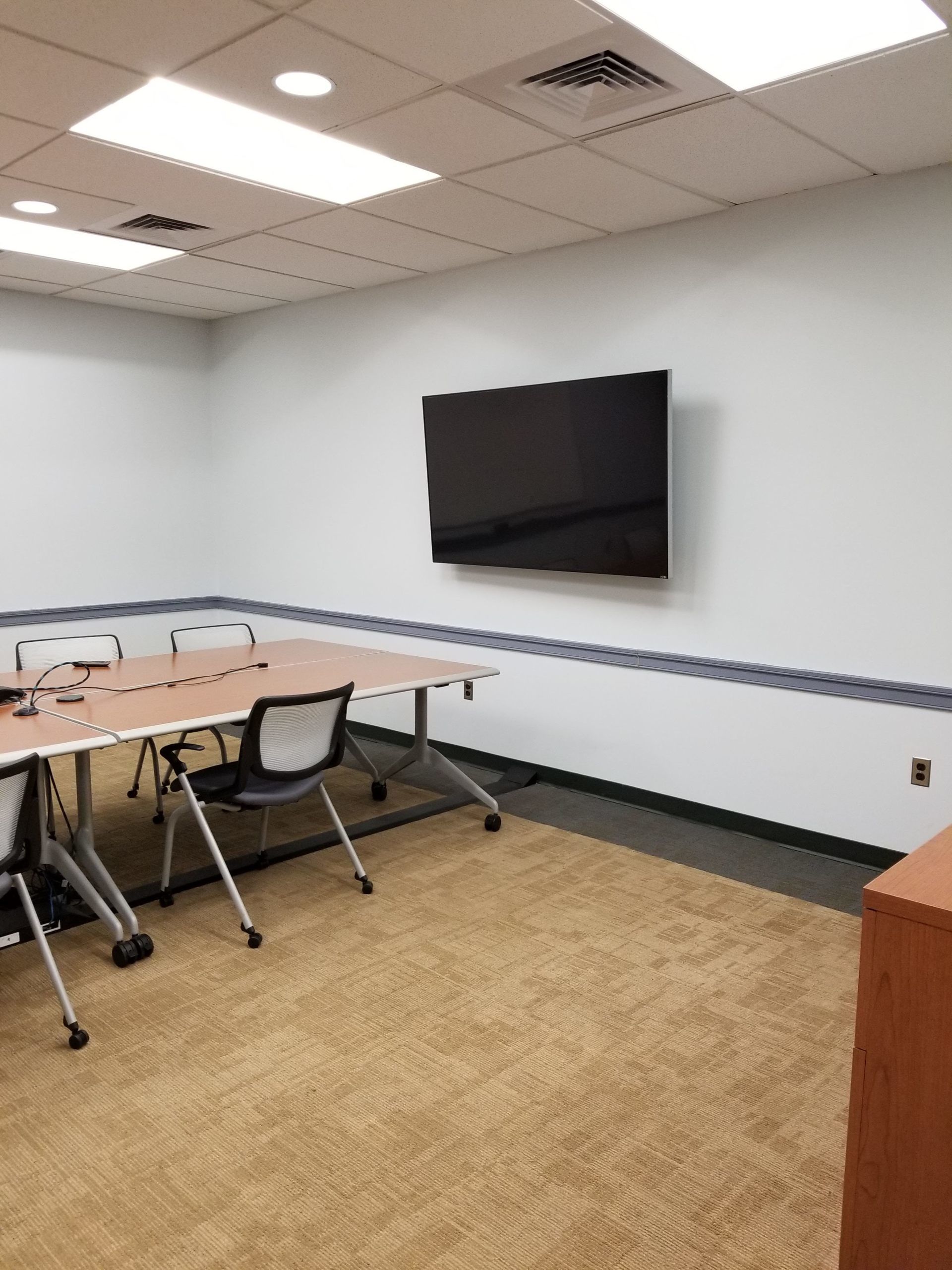 A conference room with a table and chairs and a flat screen tv on the wall.