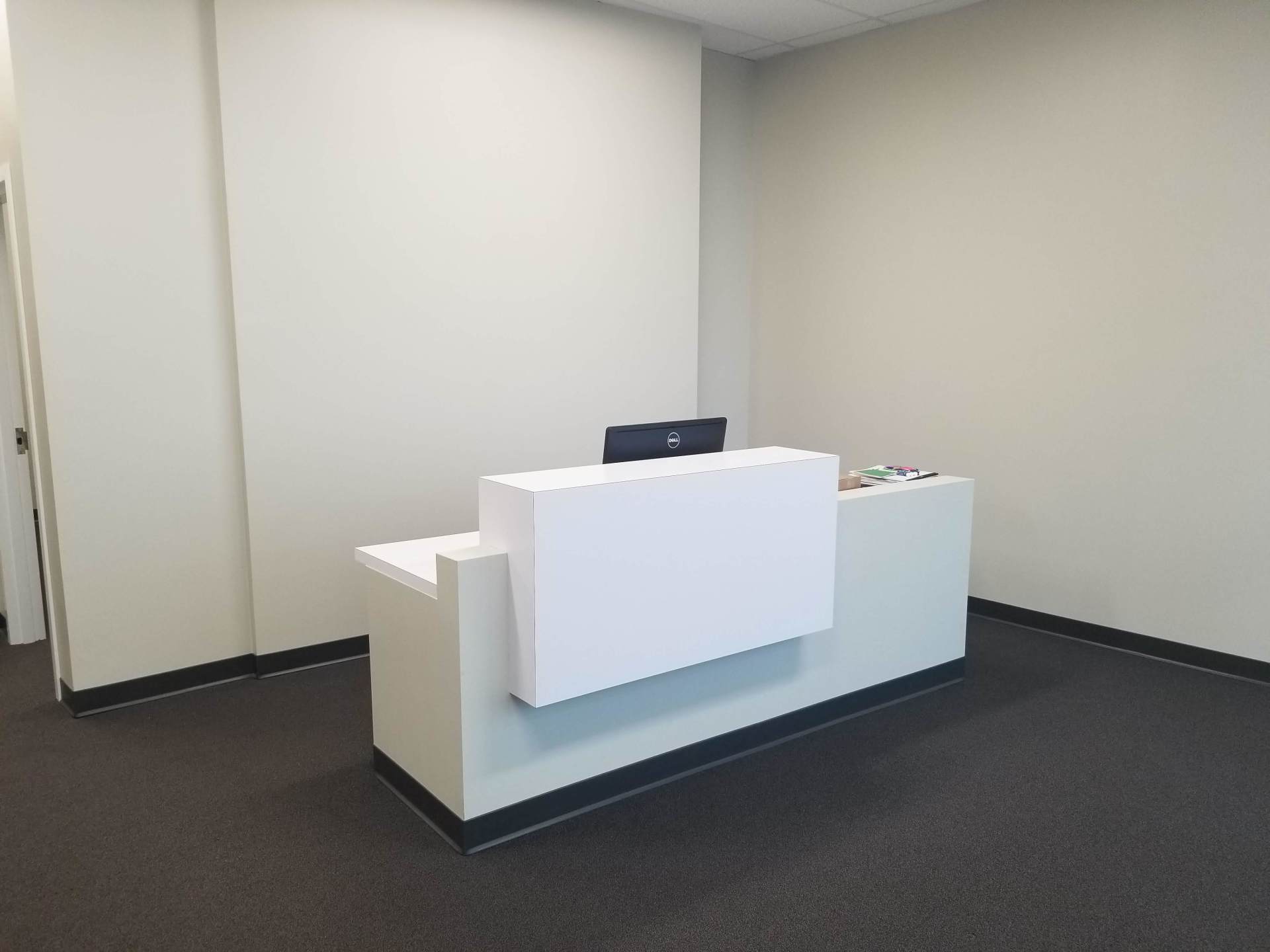 A white reception desk with a computer on it in a room.