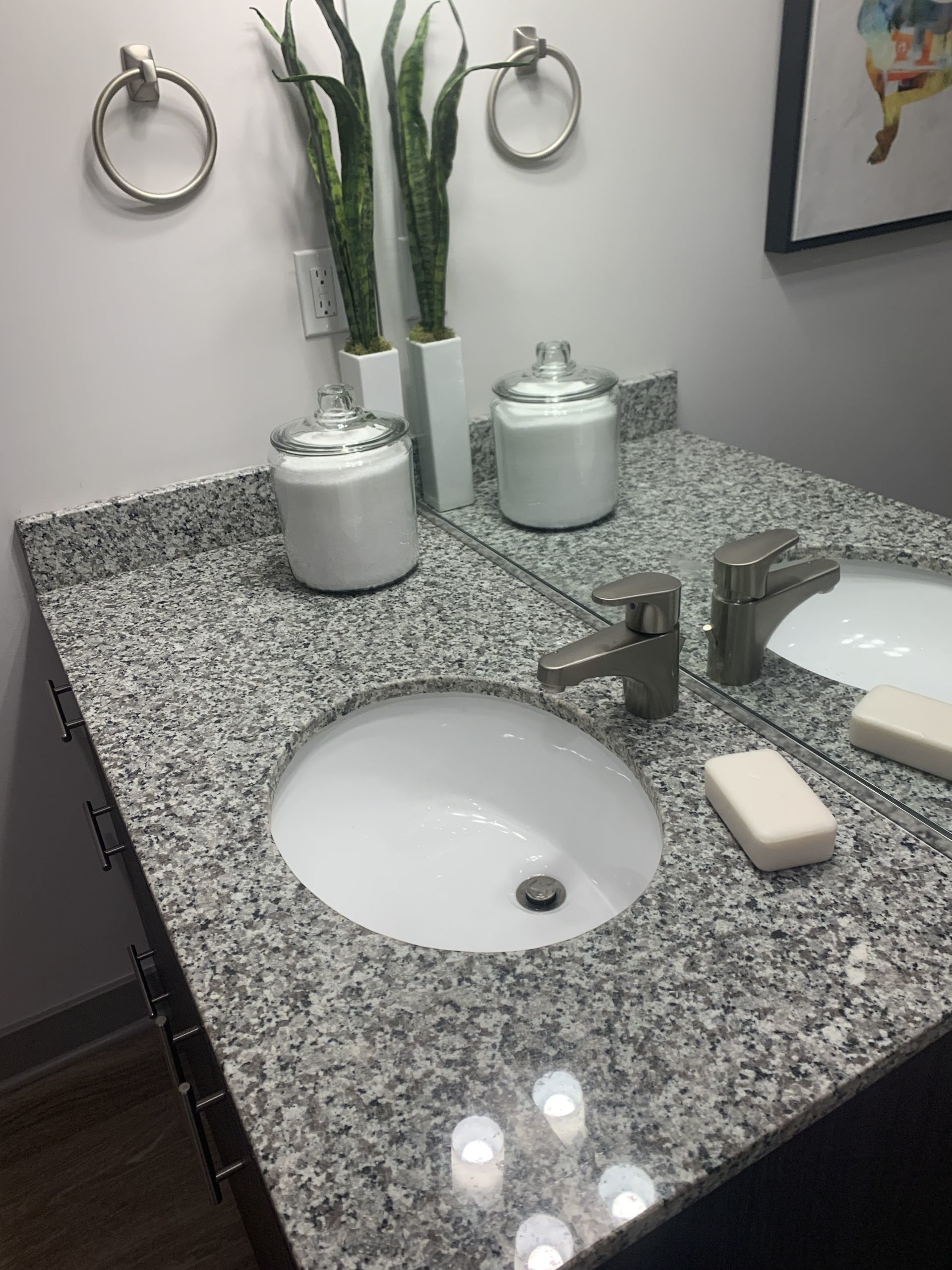 A bathroom sink with a granite counter top and a mirror.