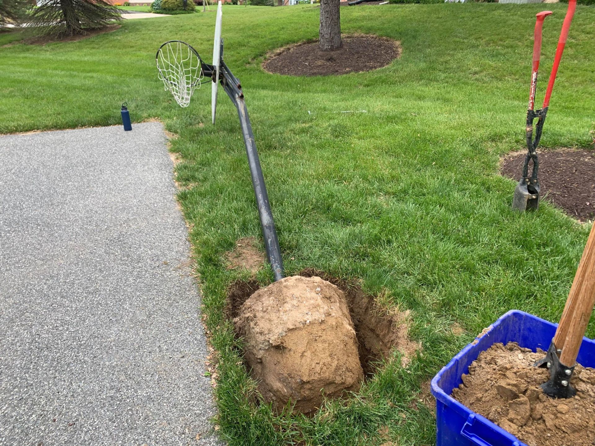 A shovel is digging a hole in the grass next to a basketball hoop.