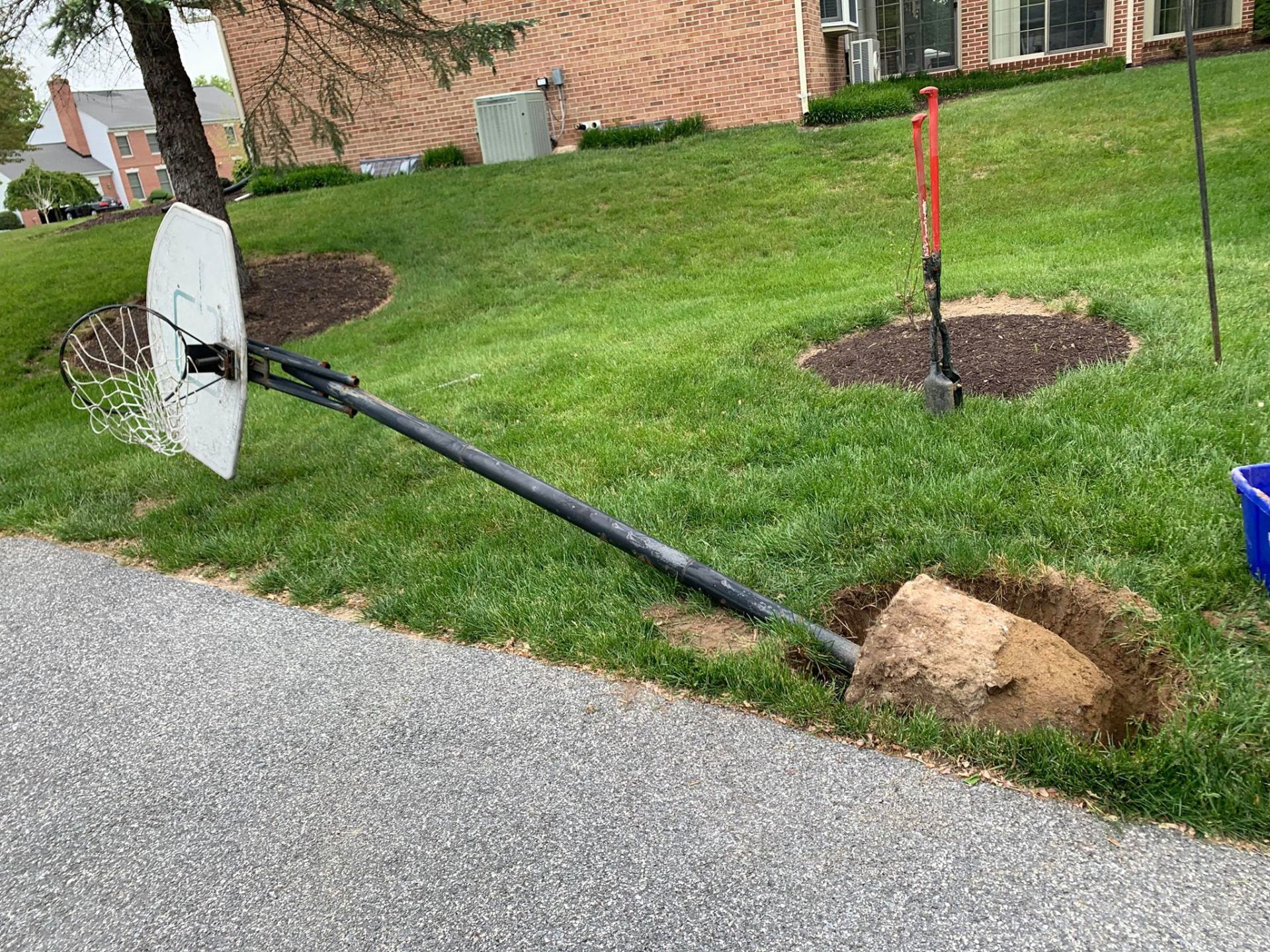 A basketball hoop is sitting on the side of the road next to a hole in the grass.