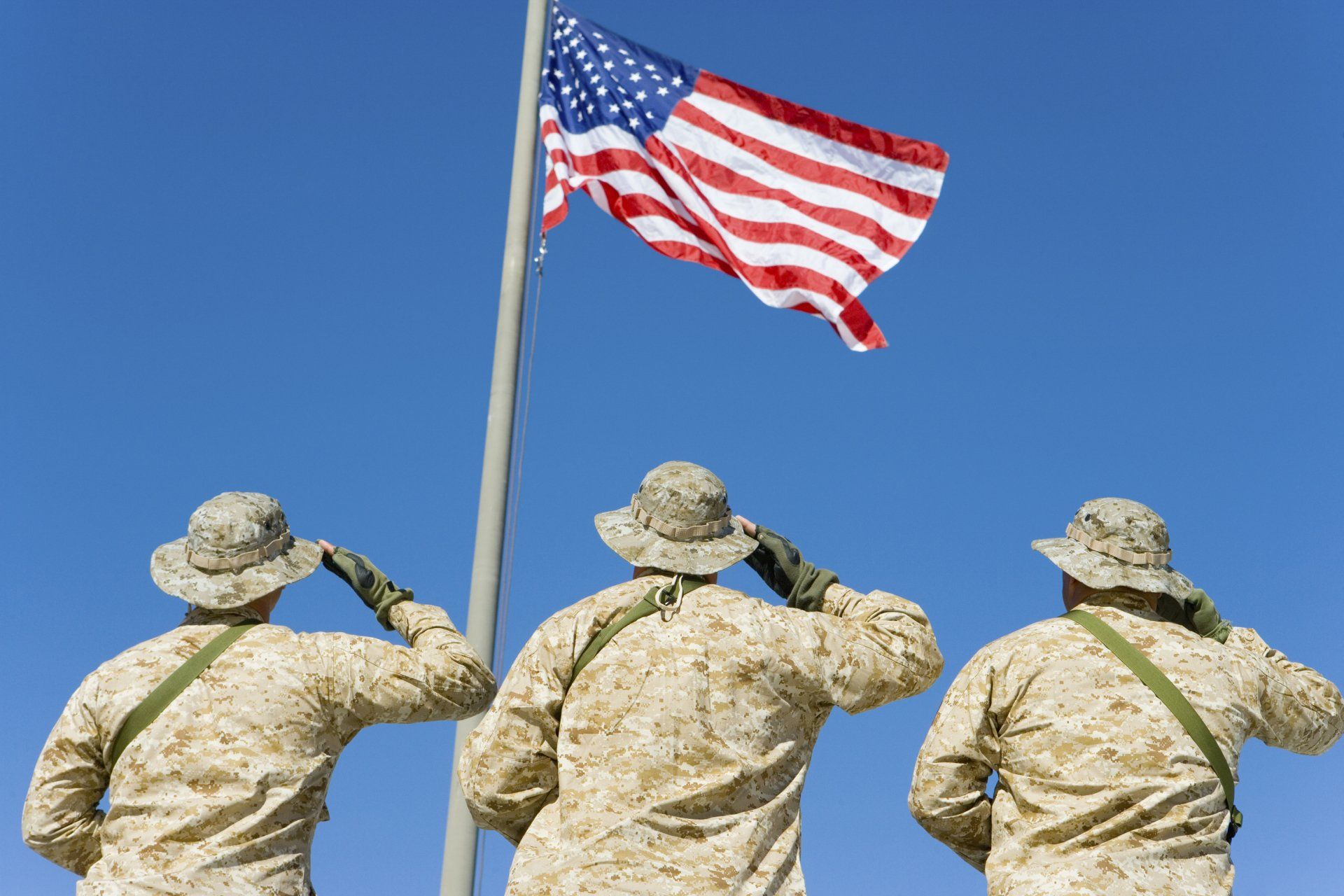 Three soldiers salute the american flag on a pole