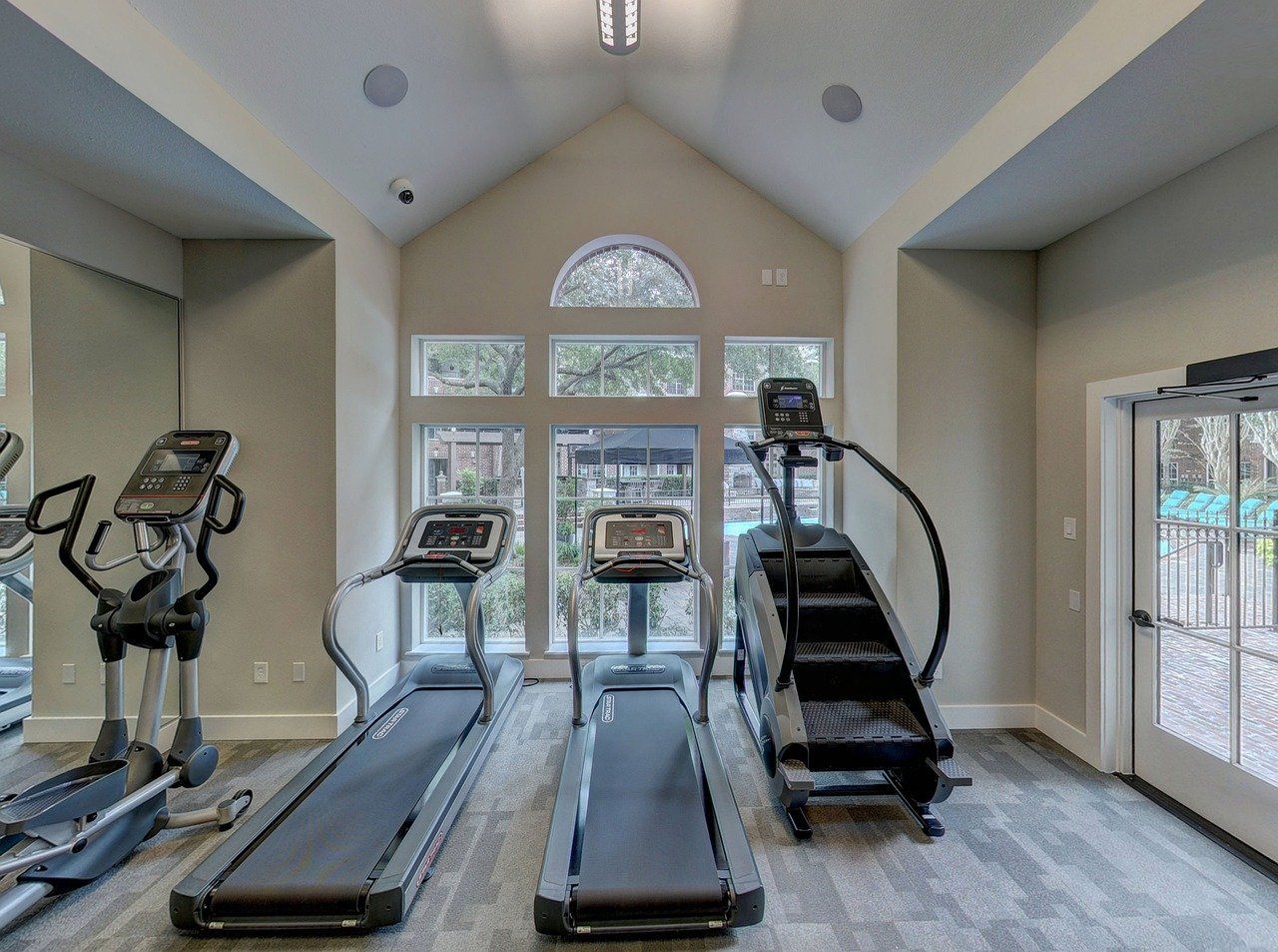 Gym interior with cardio equipment: elliptical, treadmills, stair stepper, near a window and door.