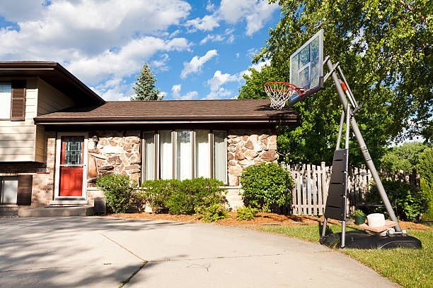 House with a red front door and a basketball hoop in the driveway on a sunny day.