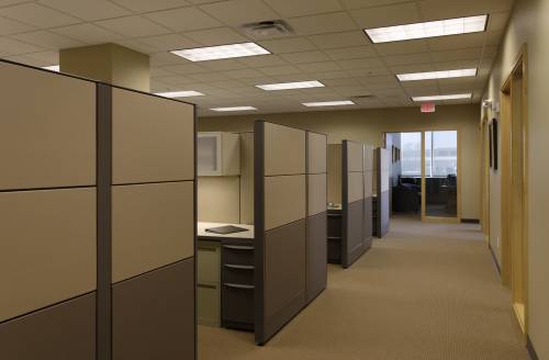 Empty office featuring rows of beige cubicles, carpeted flooring, and recessed ceiling lights.