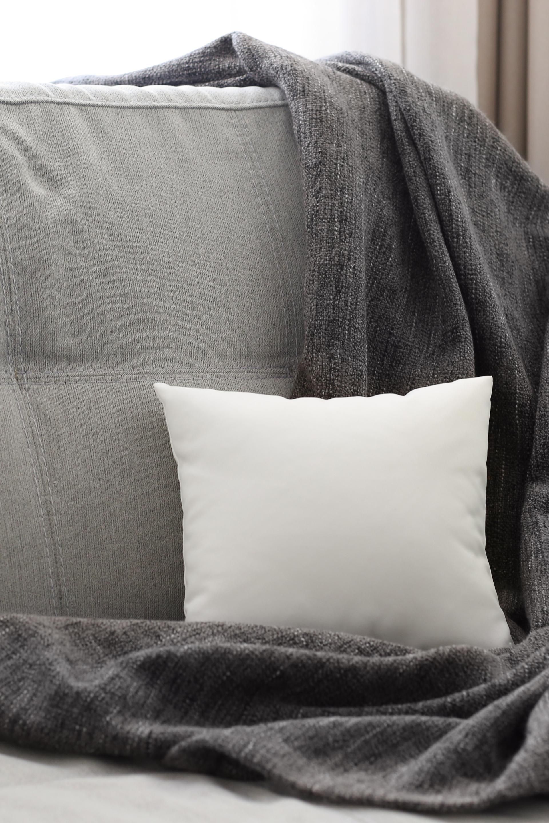 A couch with a blanket and a white pillow on it.