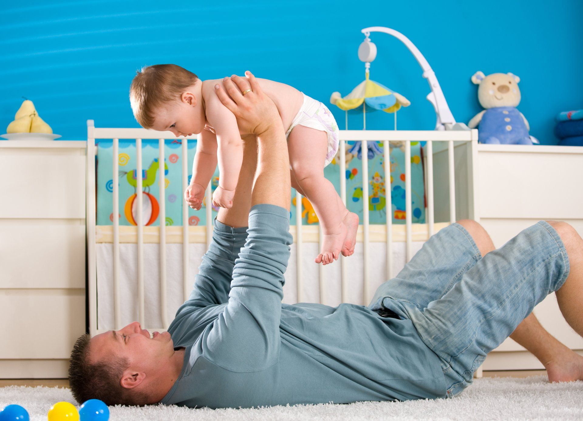 A man is laying on the floor holding a baby in the air