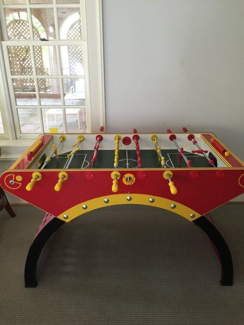 Red and yellow foosball table in front of a window.