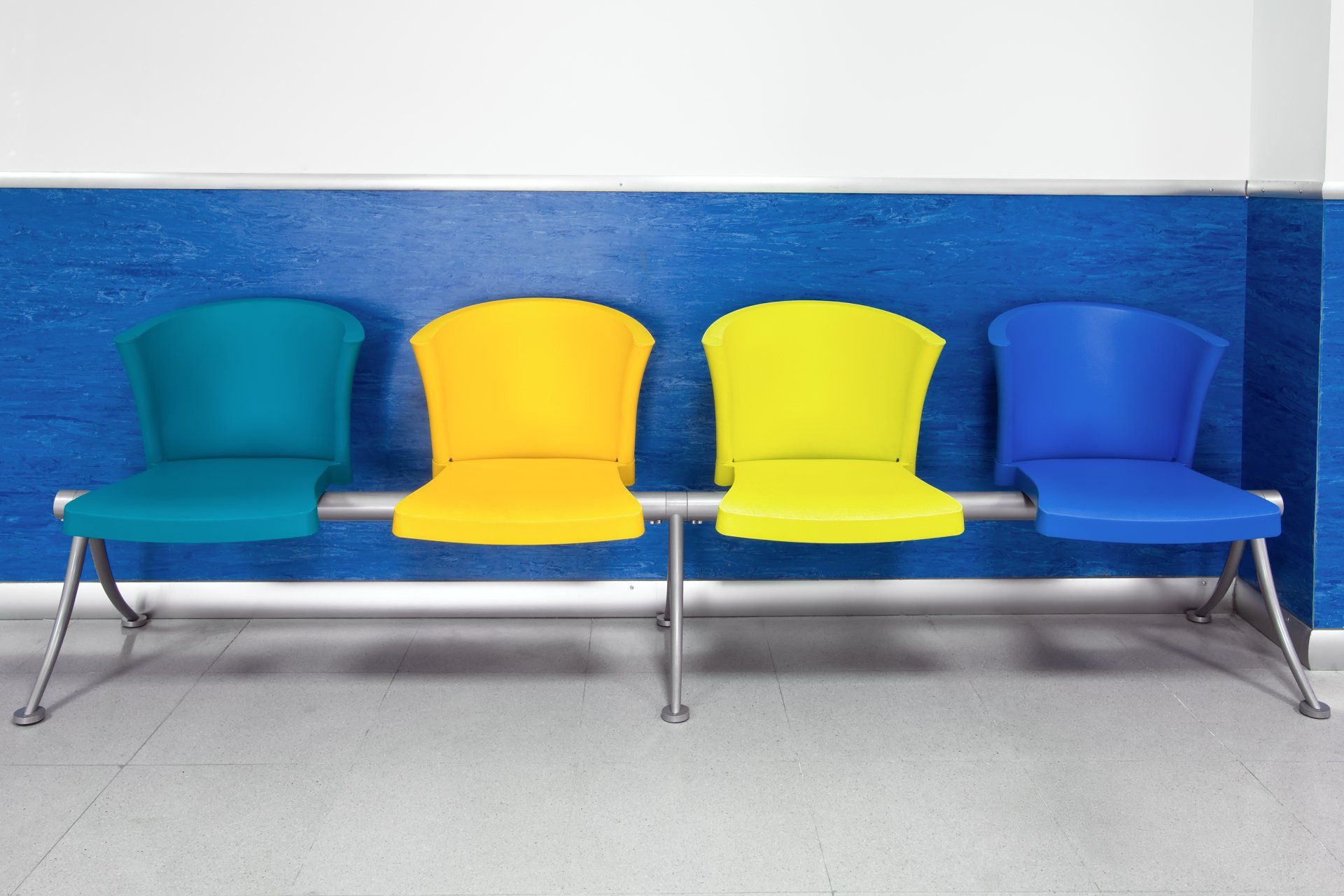 Four colorful chairs are lined up in a row against a blue wall.