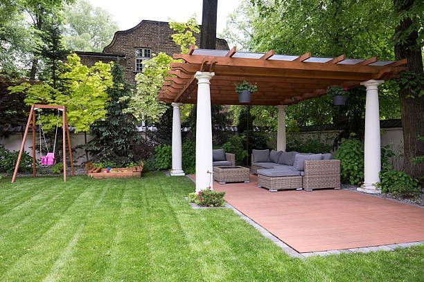 A backyard with a wooden pergola, outdoor seating, swing set, and manicured lawn.