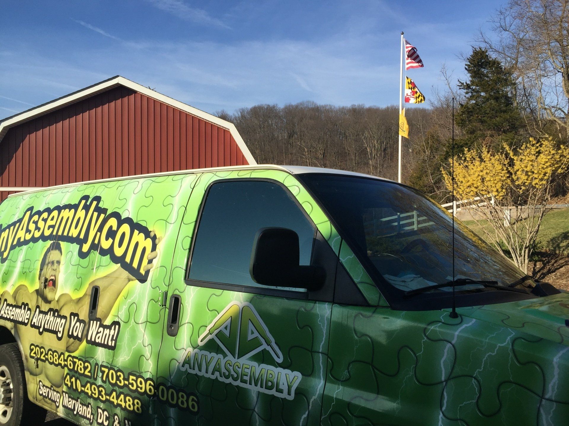A green van is parked in front of a red barn