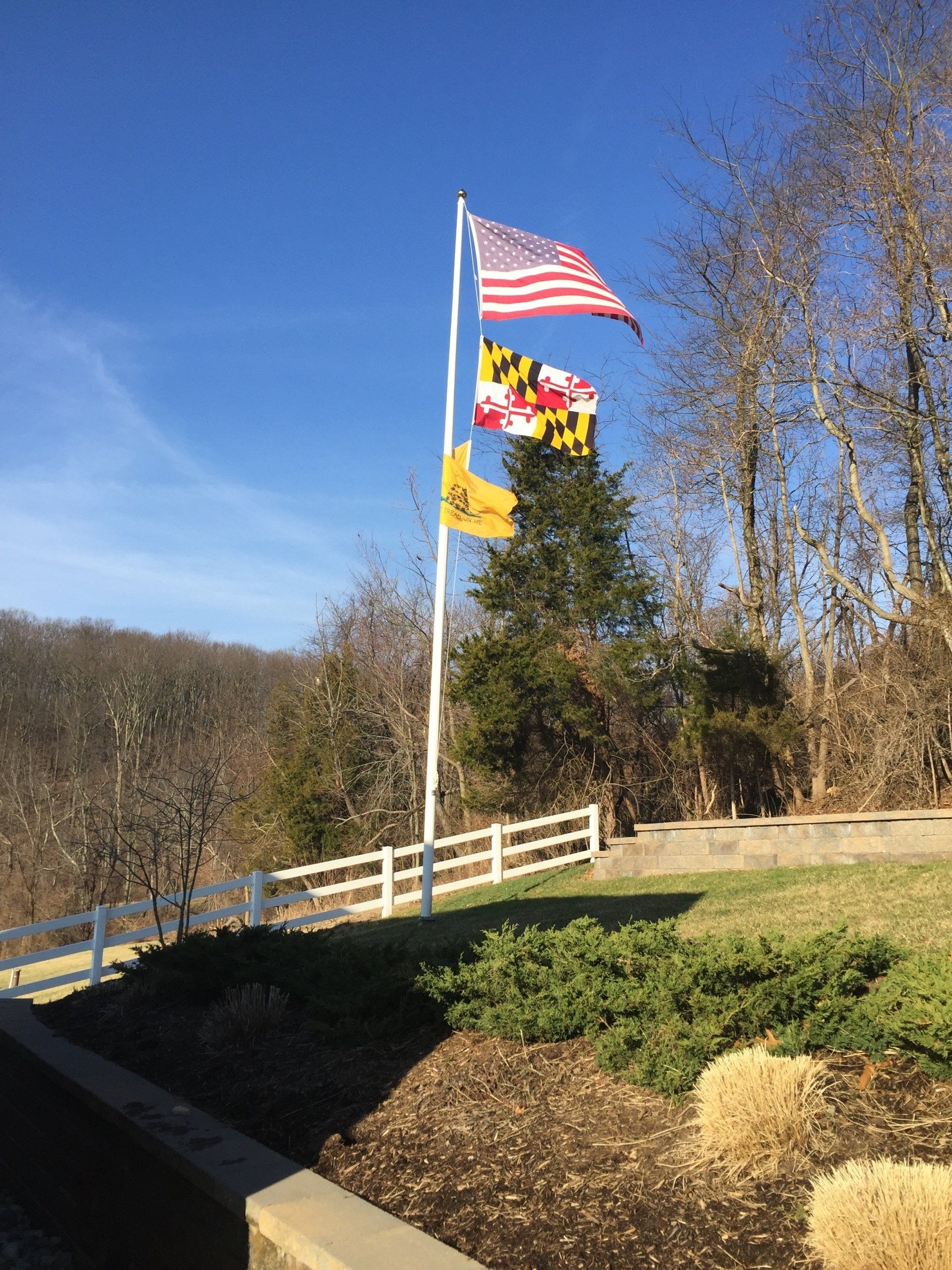 Three flags are flying on a pole in front of a fence.