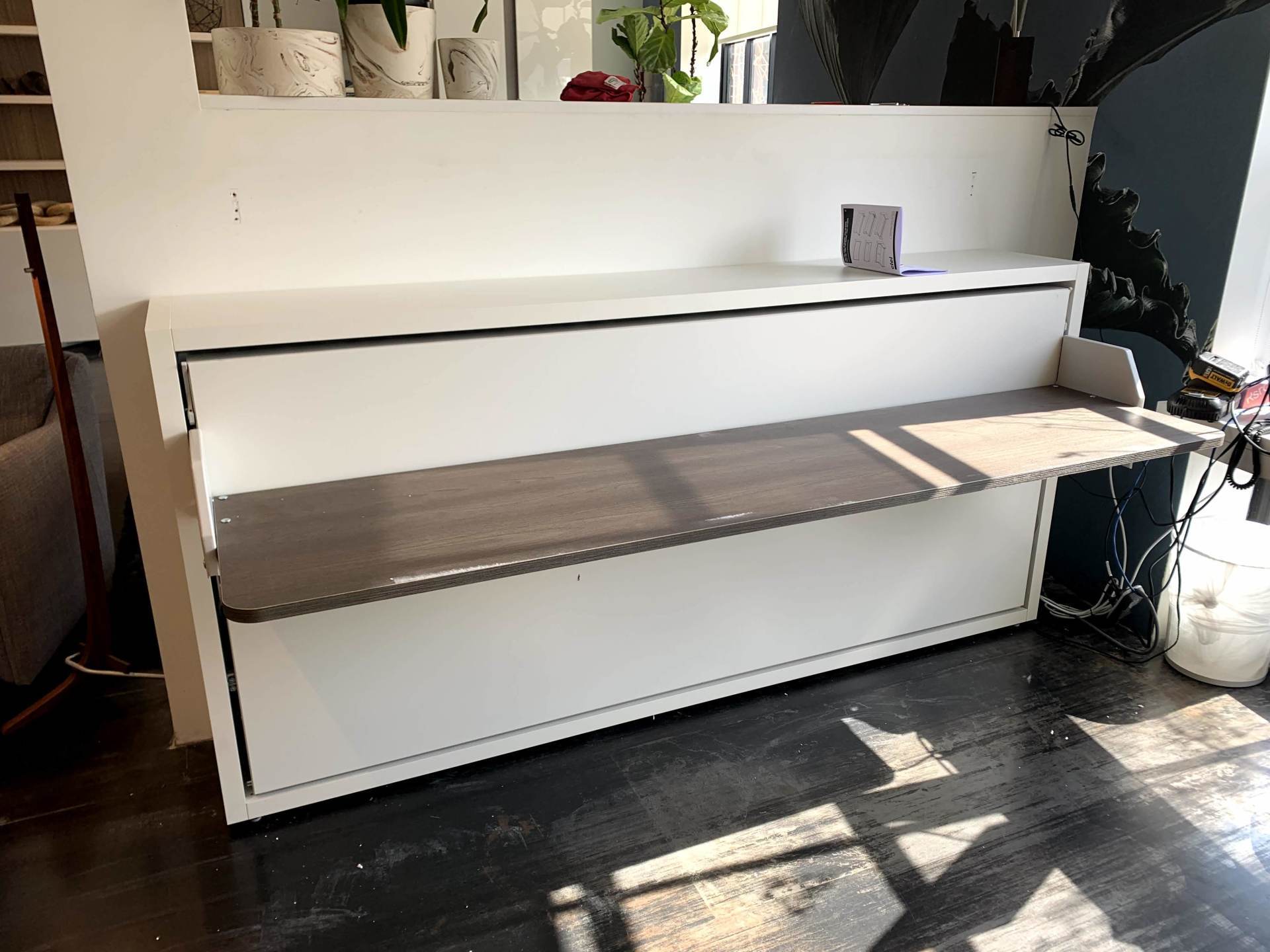 A white wall mounted desk with a wooden bench underneath it.