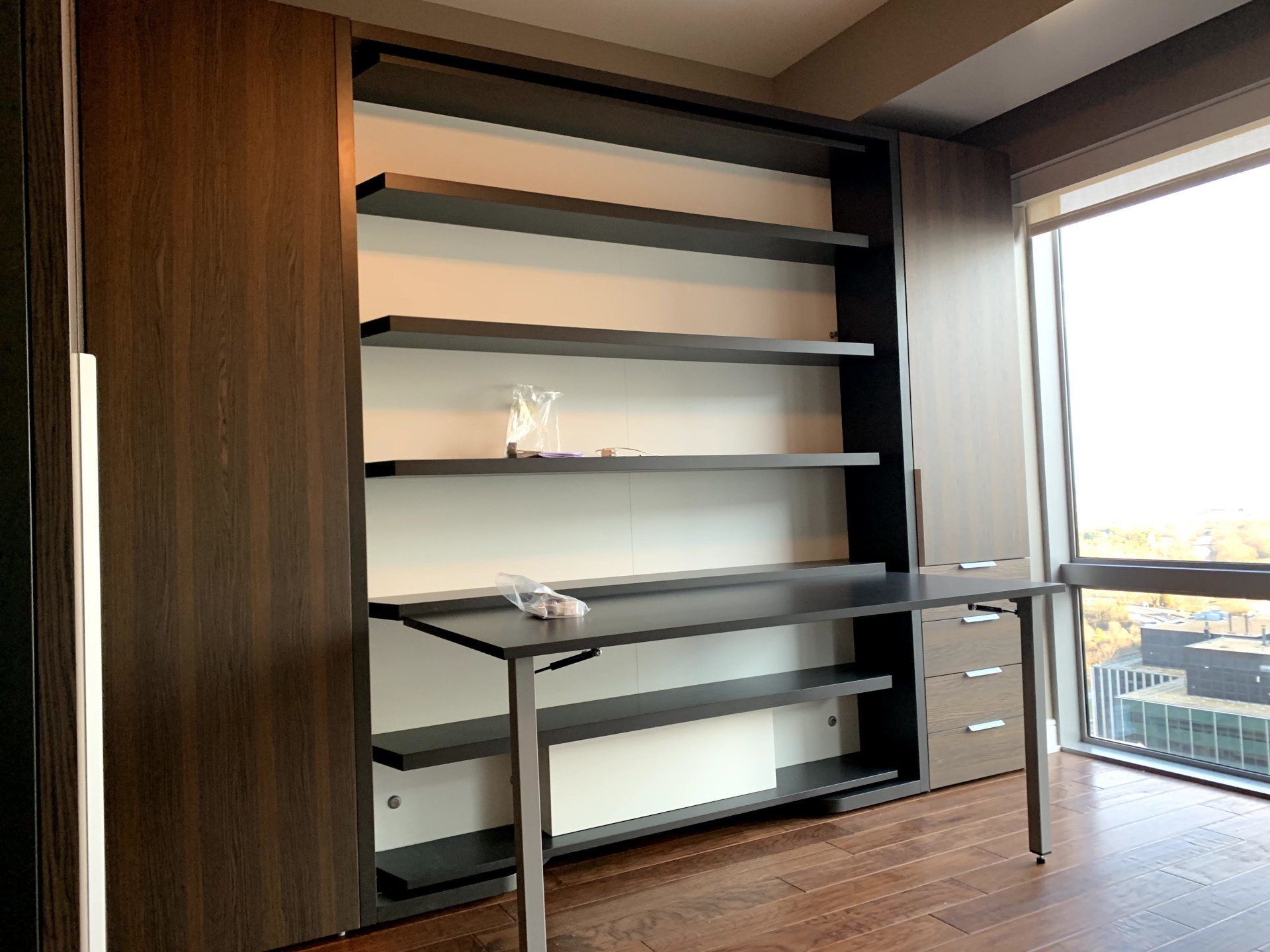 A room with a desk , shelves and a window.