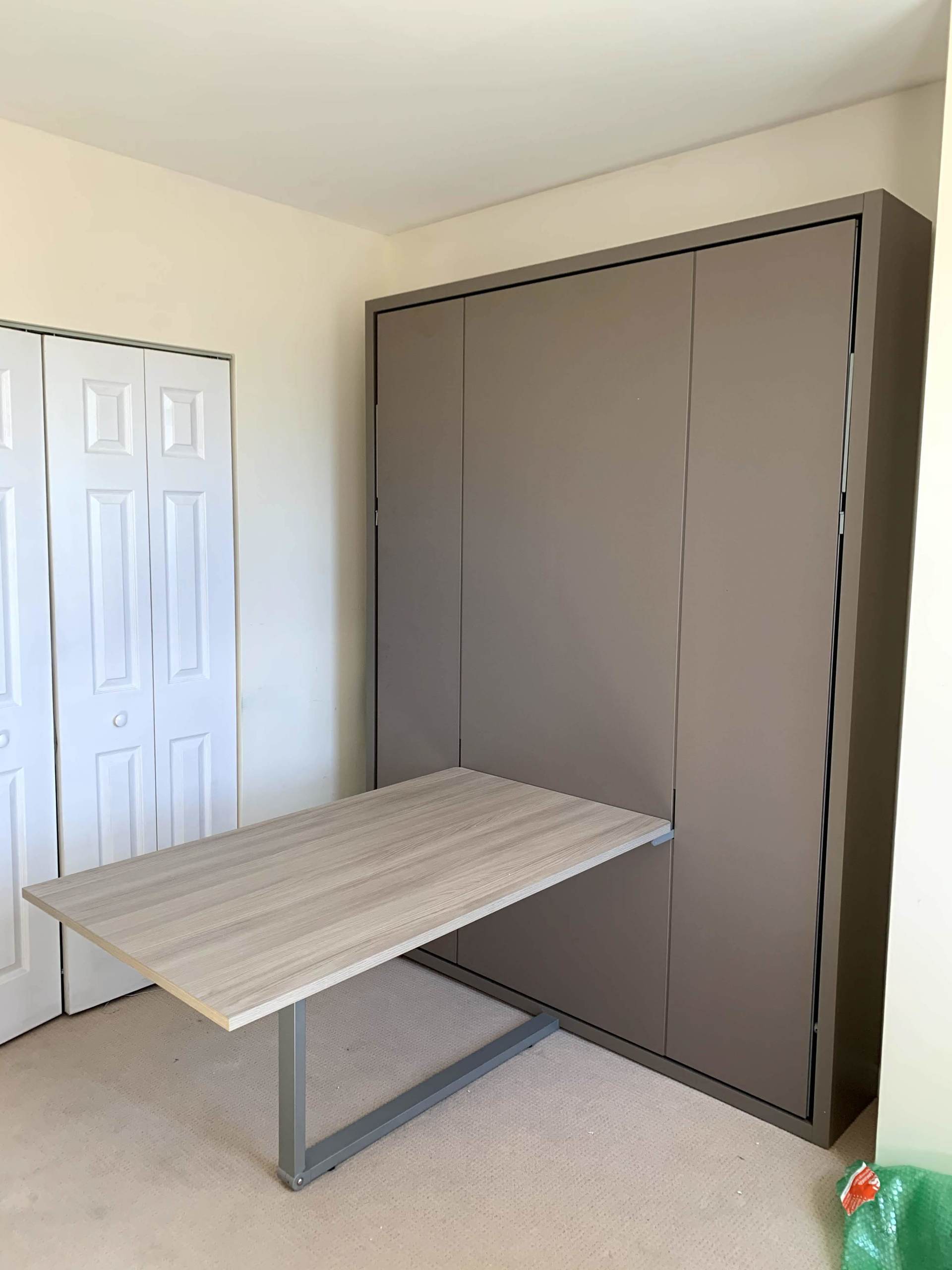A wooden table is sitting in front of a wall mounted bed.