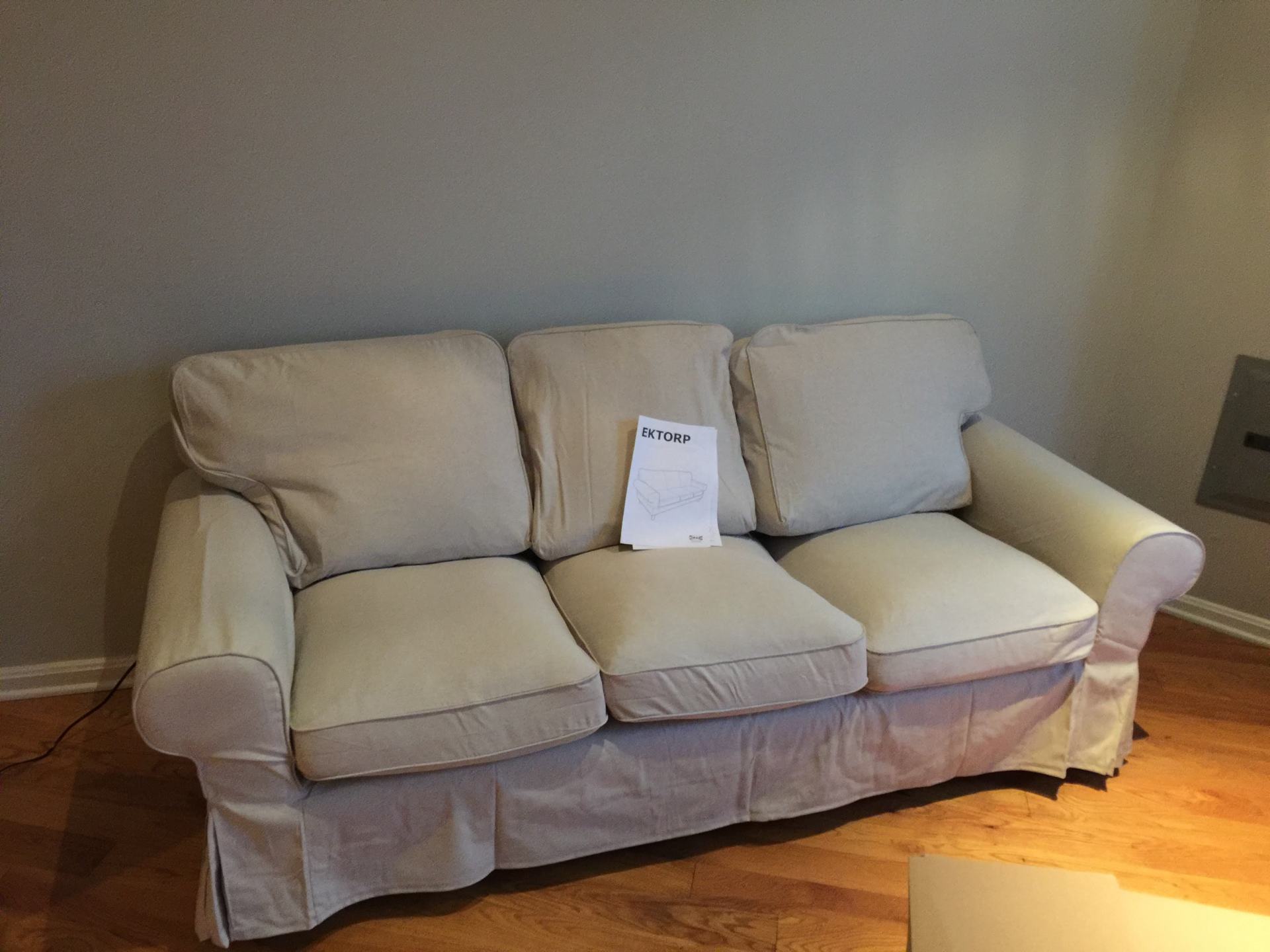 A white couch is sitting in a living room with a piece of paper on it.