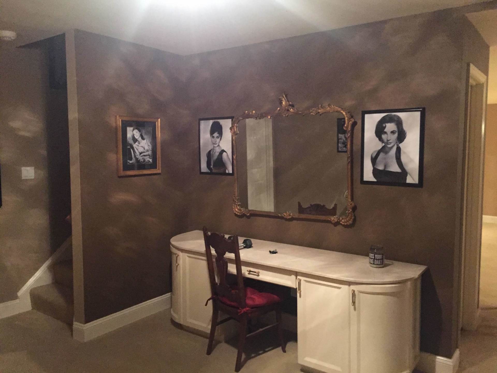 A room with a desk , chair , mirror and pictures on the wall.