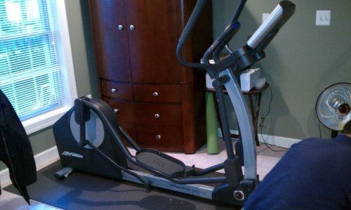 Elliptical machine in a home gym setting. A person is near the machine.
