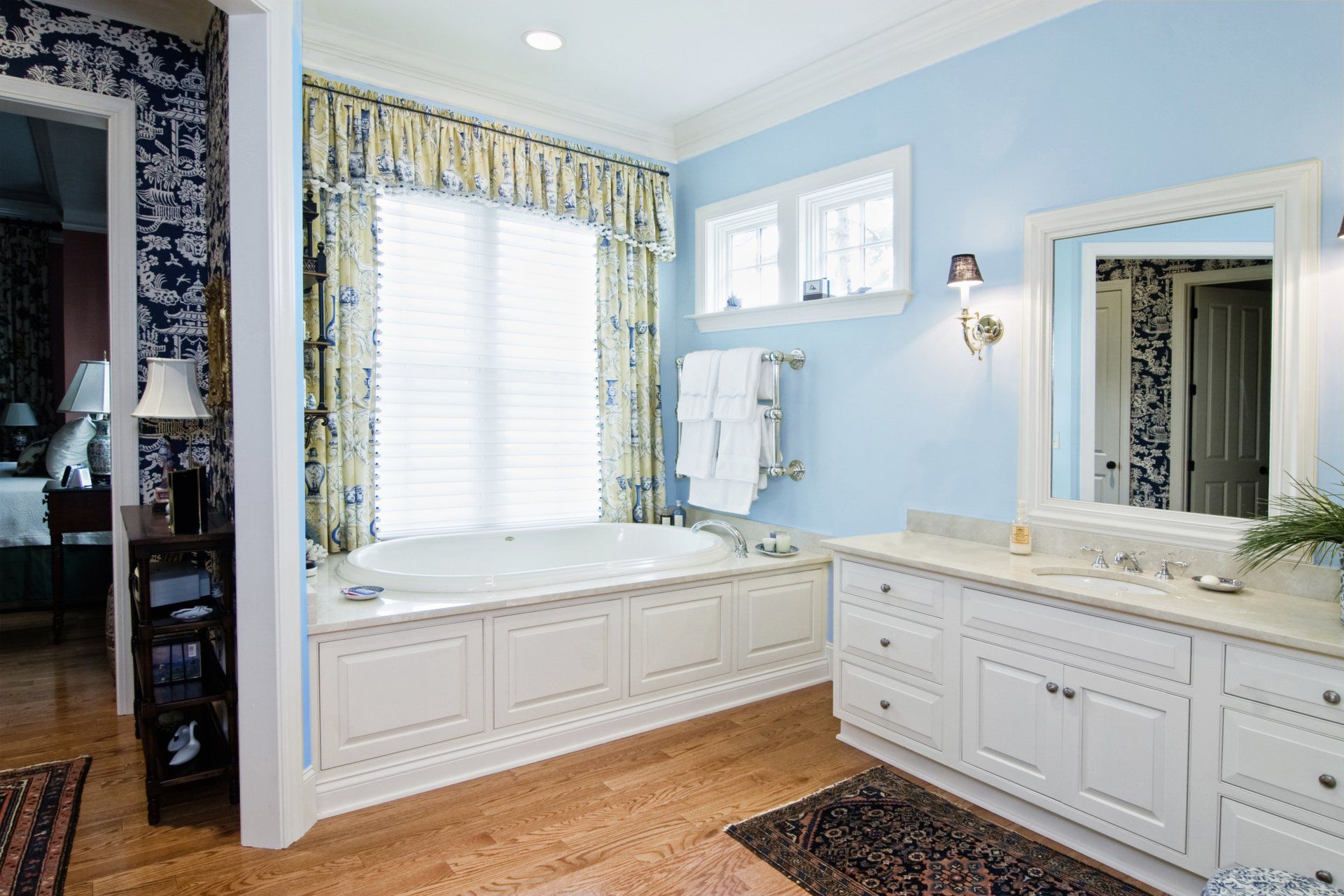 A bathroom with blue walls , white cabinets , a tub and a mirror.