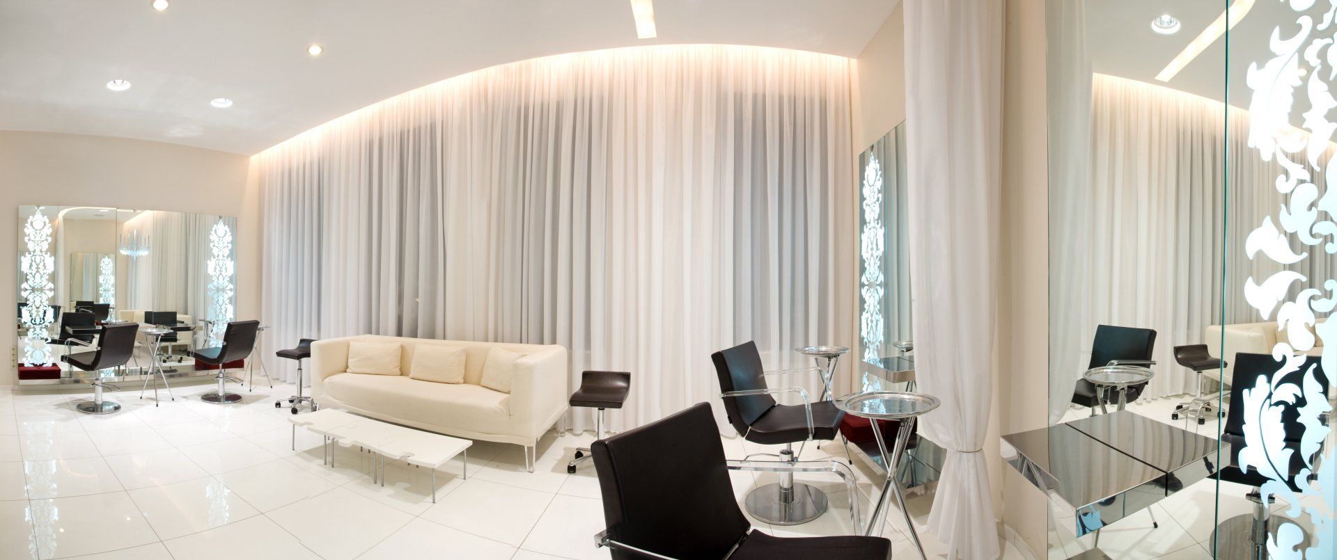 A salon with a couch , chairs , mirrors and curtains