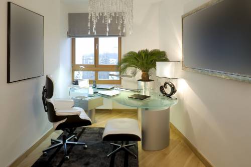 Modern home office with glass desk, chair, and art on walls.