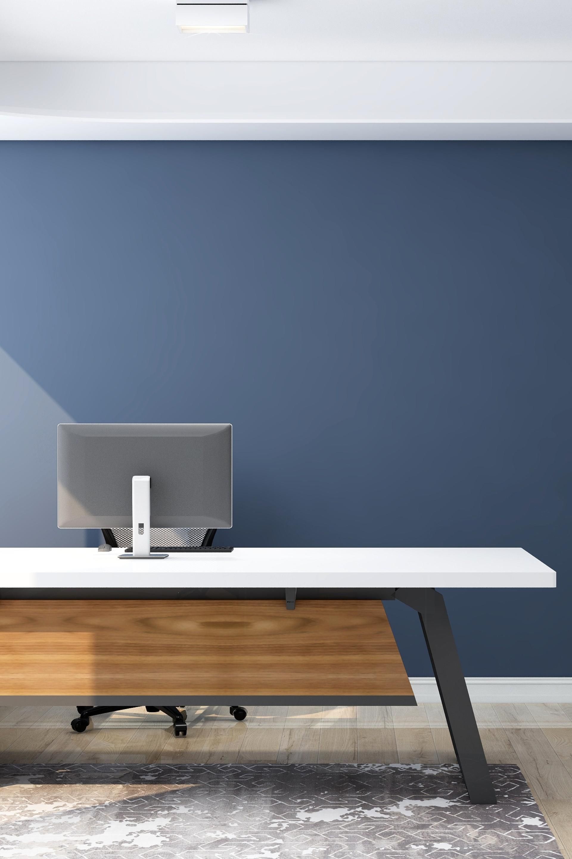 A desk with a computer on it in a room with a blue wall.