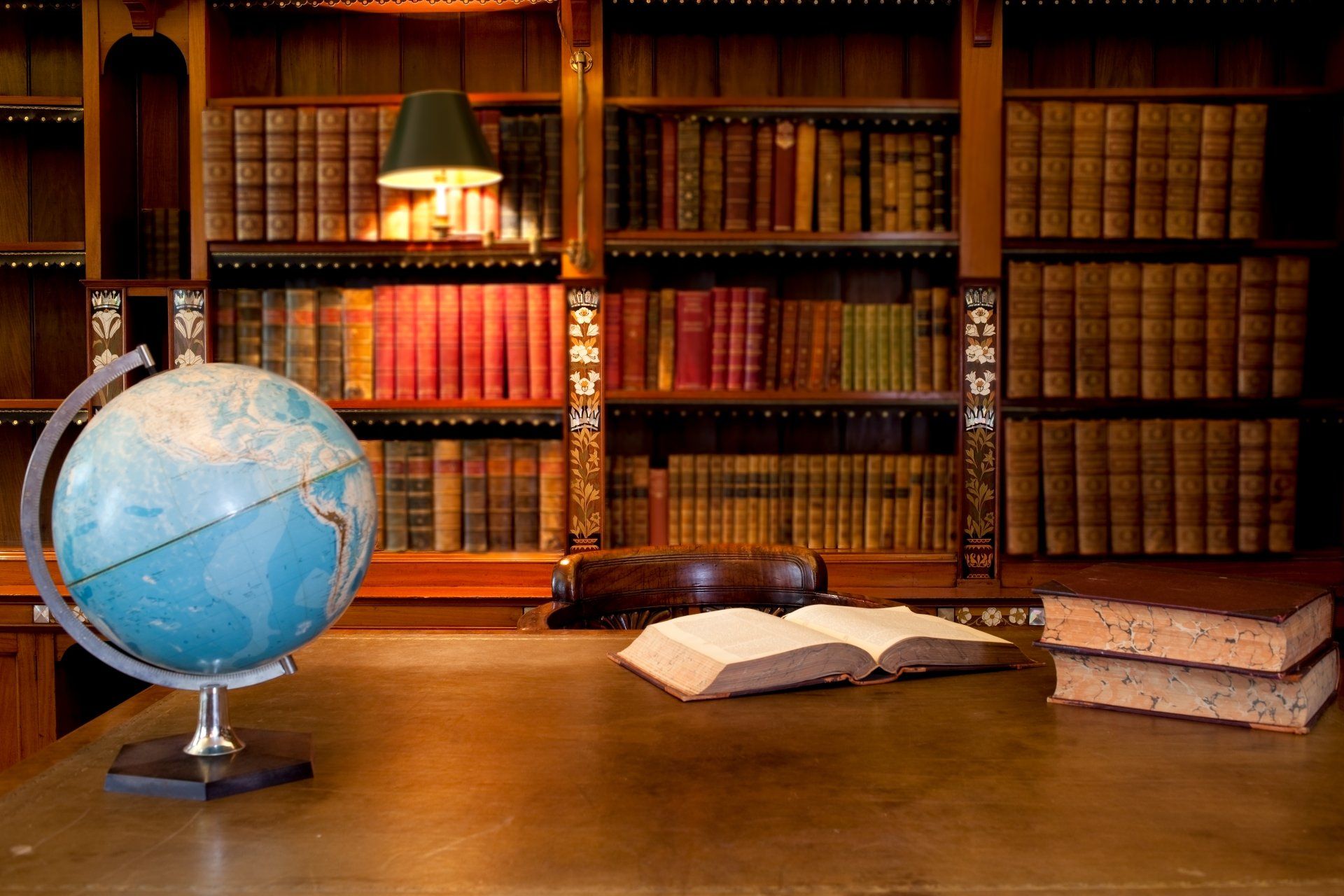 A globe is sitting on a desk in front of a bookshelf.