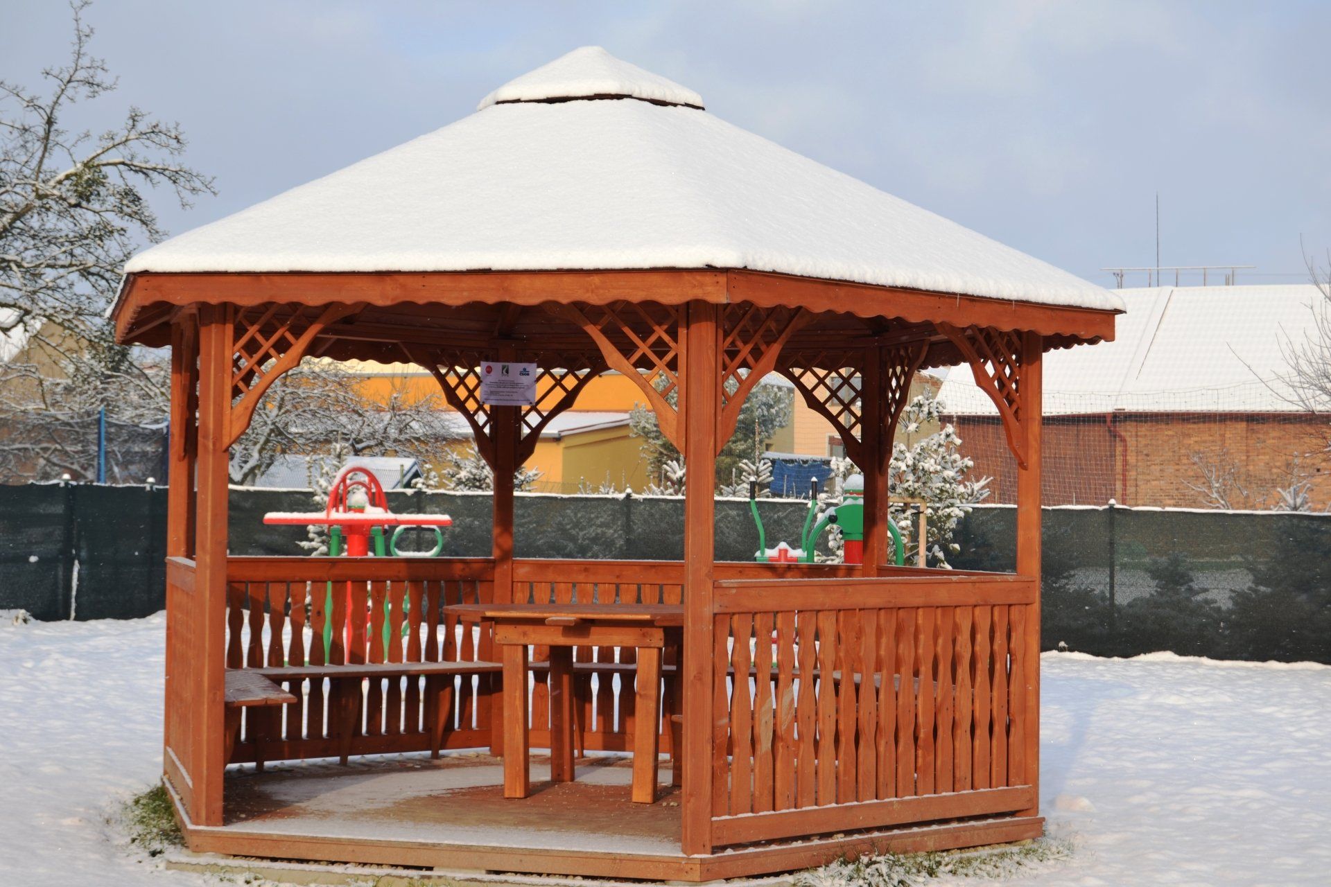 A wooden gazebo with a white roof is covered in snow