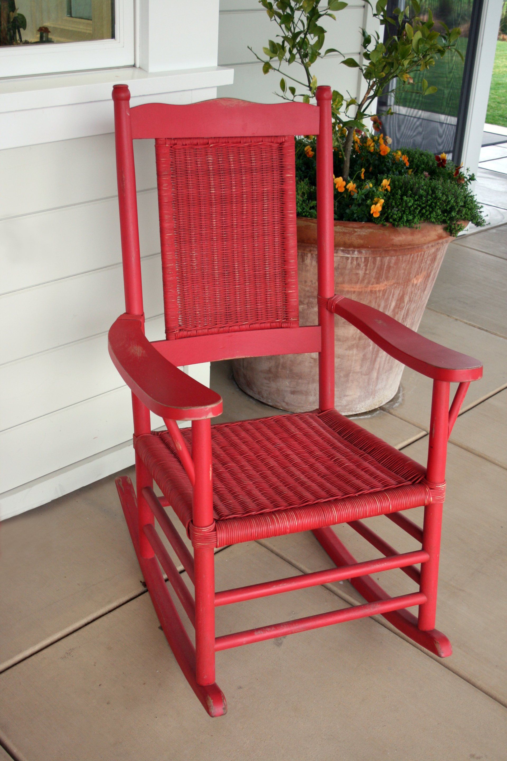 A red rocking chair is sitting on a porch next to a potted plant.