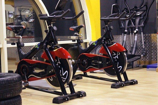 Two indoor stationary exercise bikes, black with red accents, parked on a light-colored gym floor.