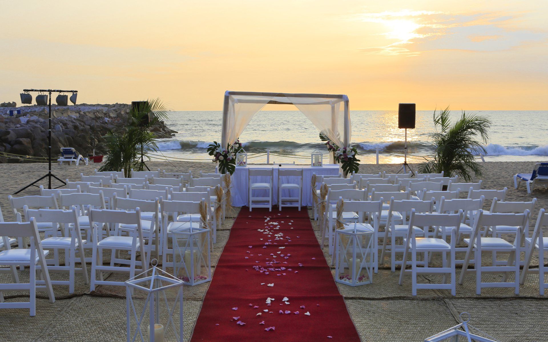 There is a red carpet leading to a wedding ceremony on the beach.