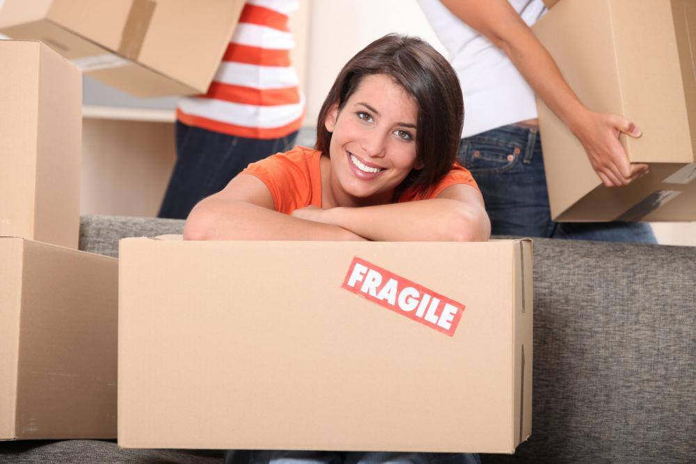 A woman is sitting in a cardboard box with a fragile sticker on it.