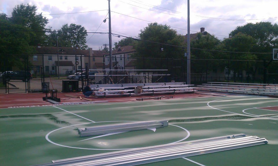 A basketball court is being built in a park with bleachers in the background.