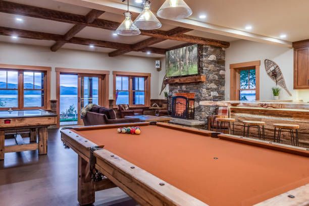 Game room with pool table, fireplace, windows overlooking a lake.