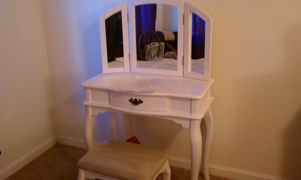 A white vanity with three mirrors and a stool in a bedroom.