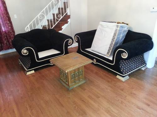 Two ornate black armchairs and a small table on a wood floor, near a staircase.