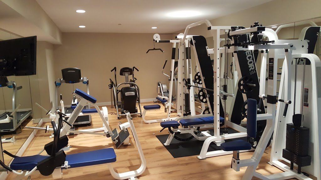 A home gym featuring various exercise machines, including weight stations and a treadmill, on a wooden floor.