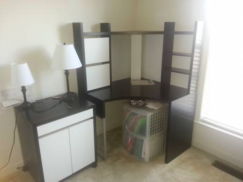 A black and white corner desk with shelves and cabinets, and a side table with lamps.