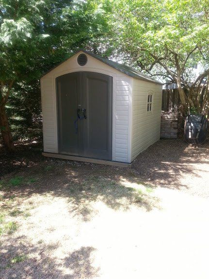 A white shed is sitting in the middle of a yard surrounded by trees.