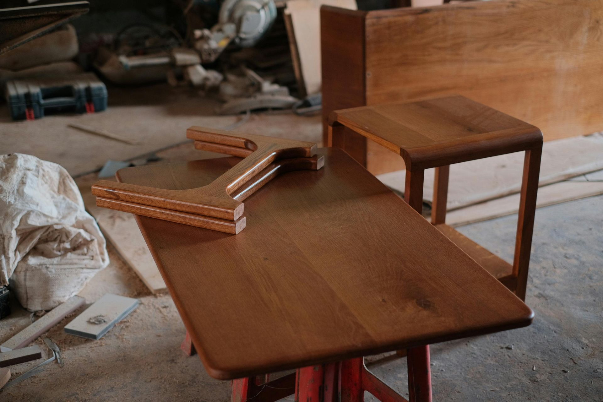 Wooden furniture pieces in a workshop, including a small table and bench, on a dusty floor
