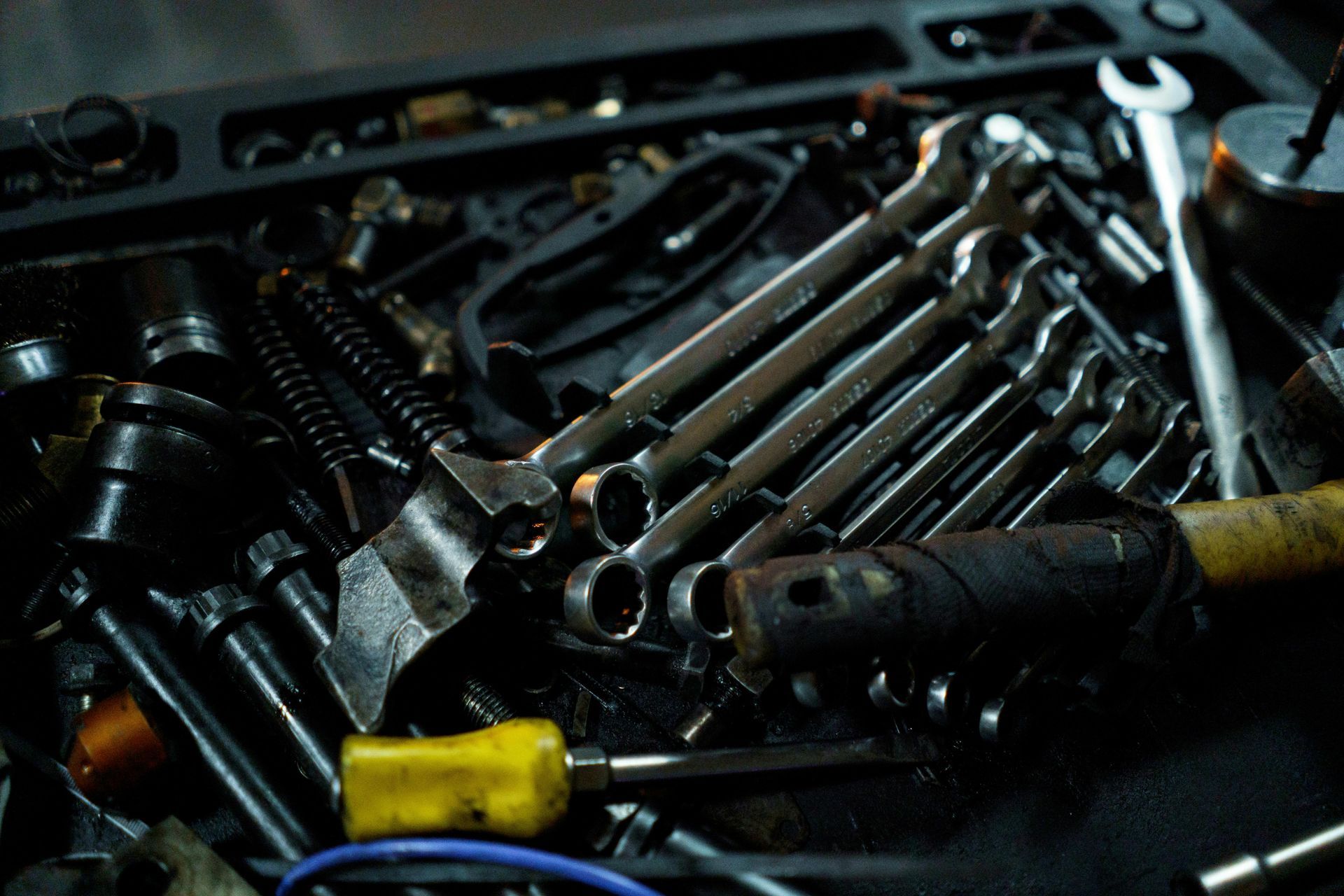 A cluttered workspace filled with an assortment of metallic wrenches, screws, and a screwdriver with a yellow handle.