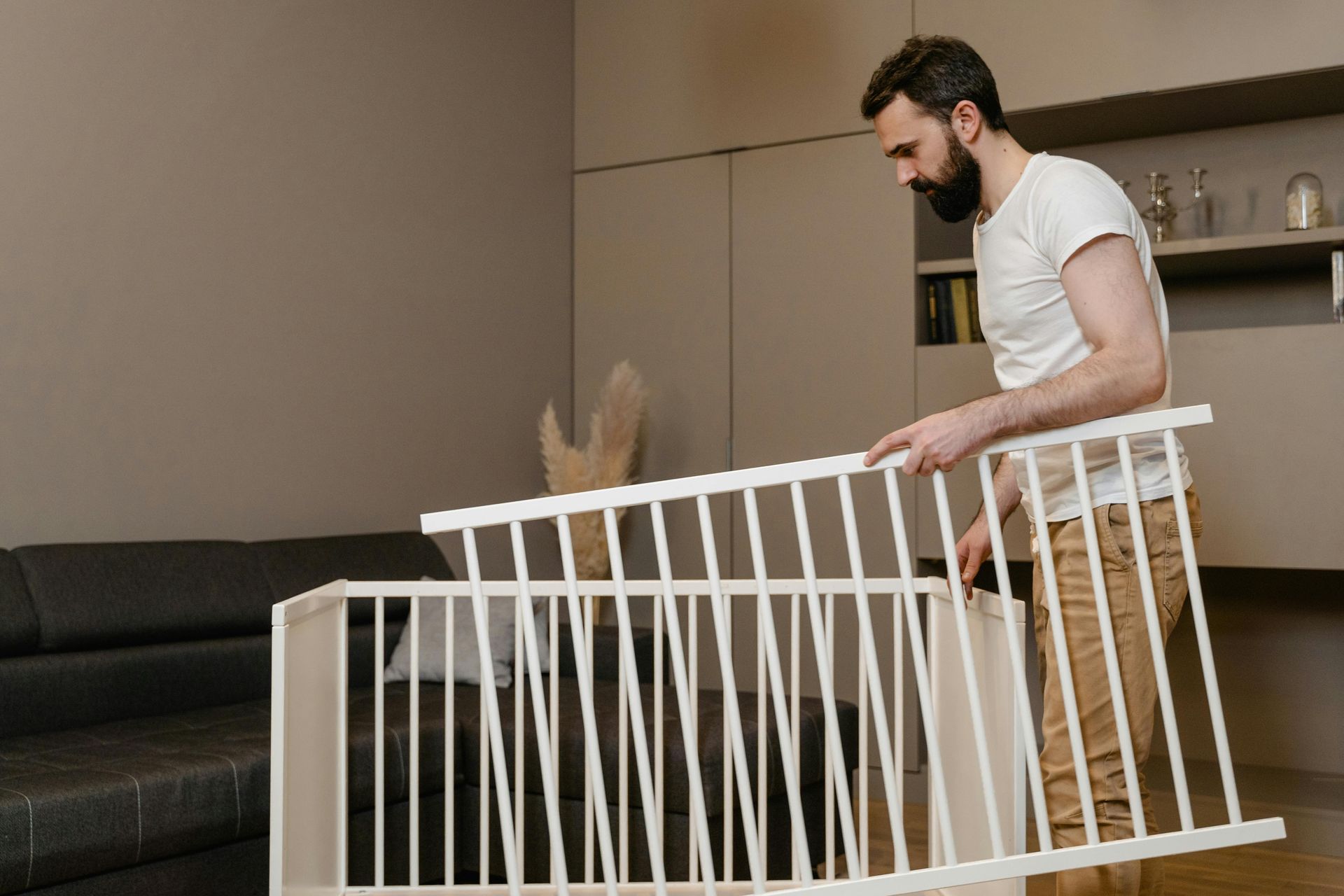 Man assembling a white crib in a living room.