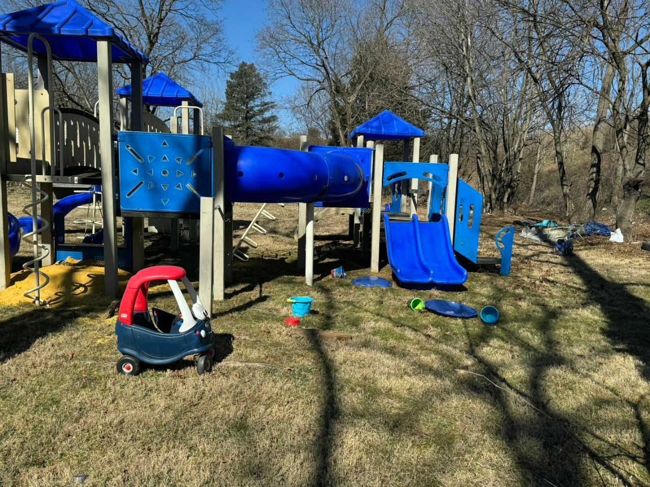 A colorful outdoor playground structure with blue slides and tunnels, alongside a small toy car on a grassy field.