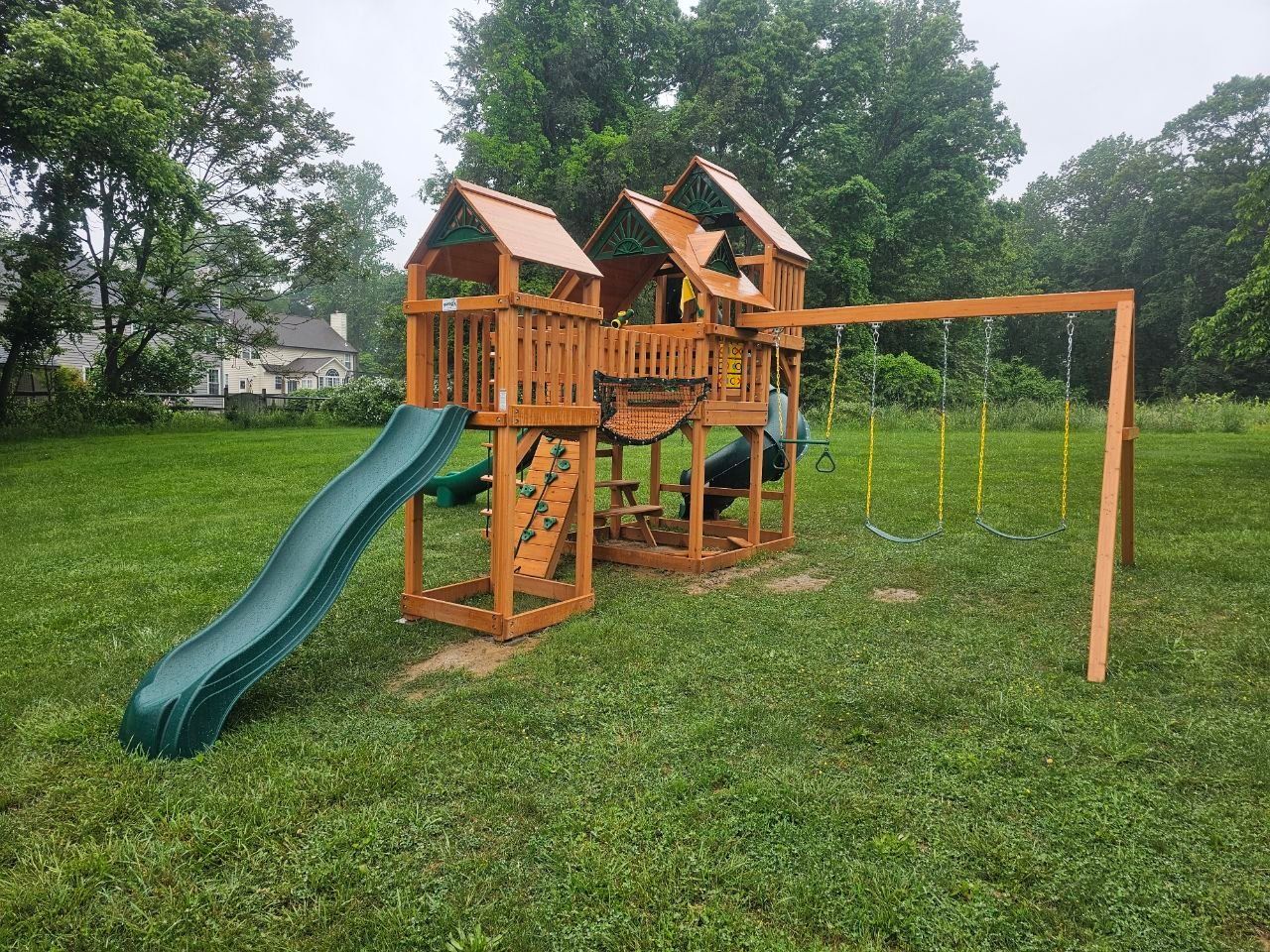Wooden playset in a grassy yard, featuring a slide and swing set.