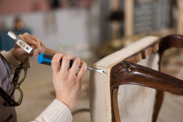 Hand using a hammer and screwdriver to repair a wooden chair frame