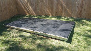 A wooden deck is sitting on top of a lush green lawn next to a wooden fence.