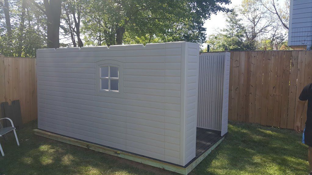 A white shed is sitting in the grass next to a wooden fence.