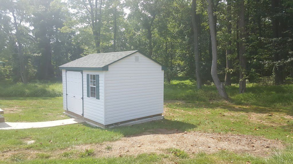 A small white shed is sitting in the middle of a grassy field.